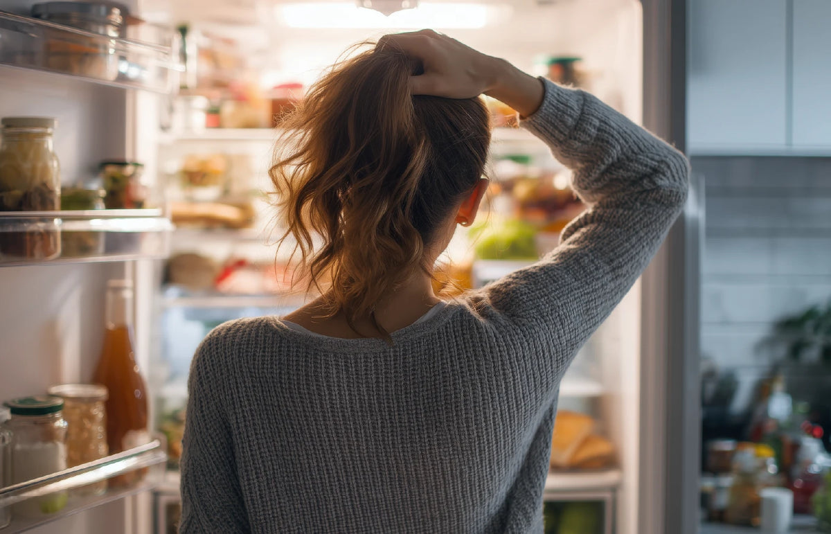 Frustrated woman standing in front of an open fridge during a craving moment