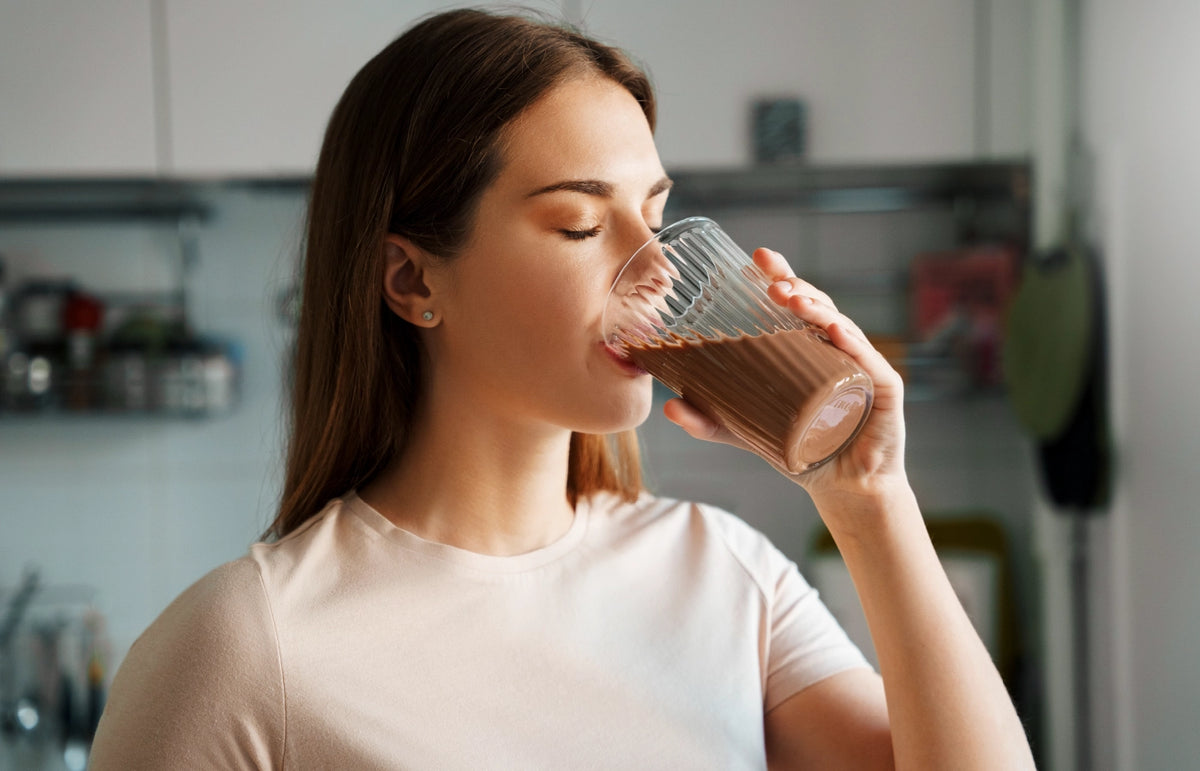 Woman drinking Athonix OFFSET Chocolate Bliss from a clear glass in her kitchen
